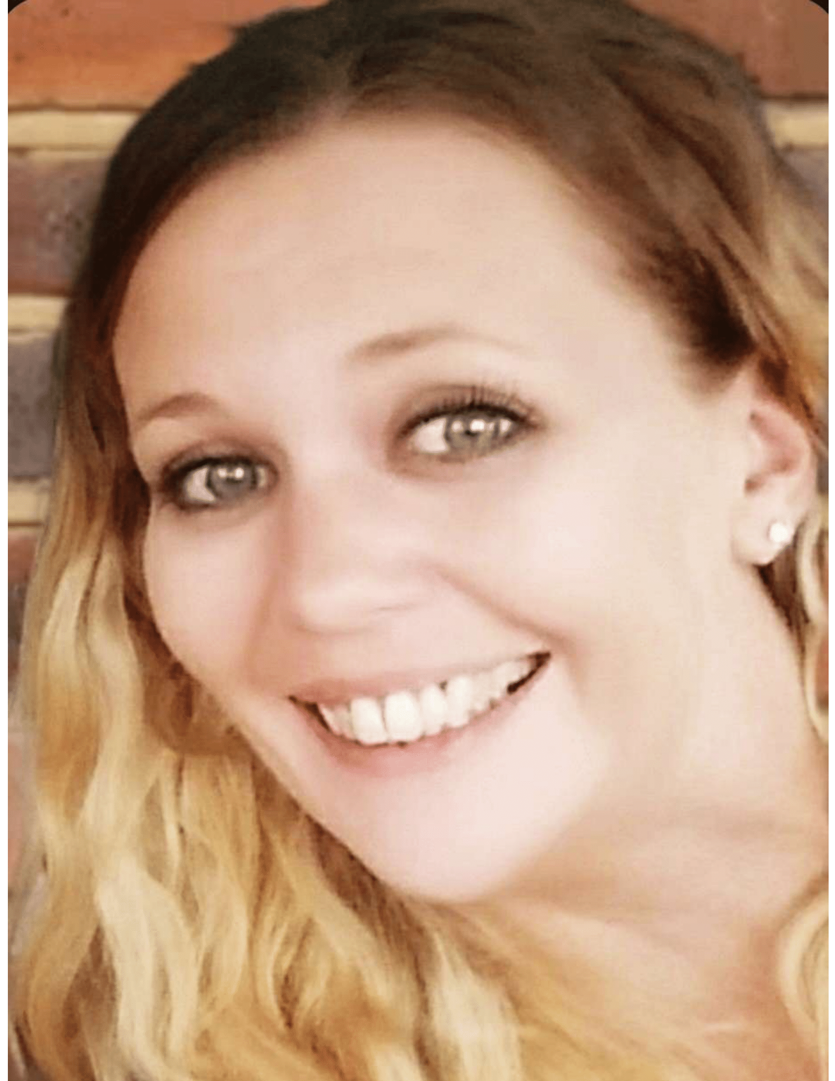 Woman with blonde curly hair smiles, gray eyes, facing camera.