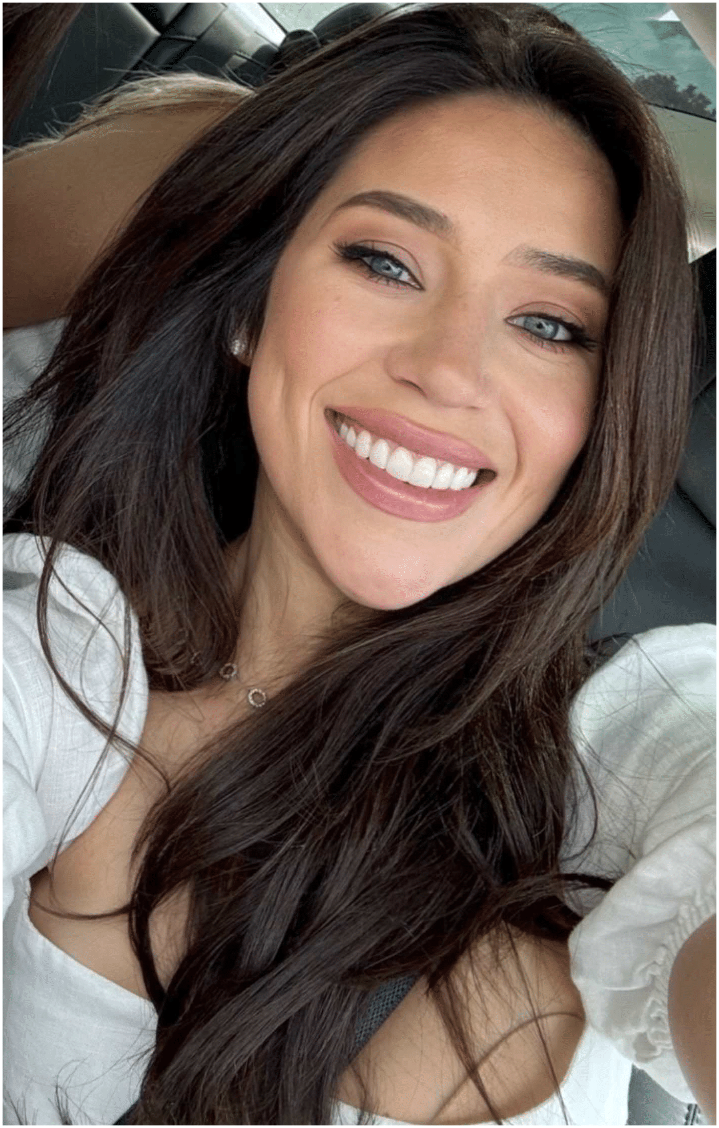 Woman with long dark hair smiles, wearing a white top.