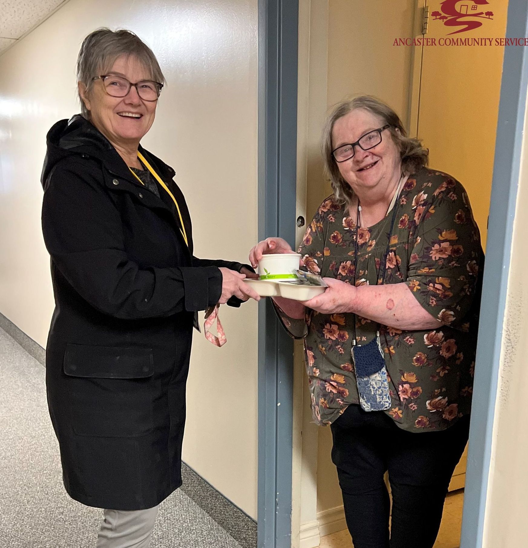 Two women are standing in a hallway and one is holding a cup of coffee