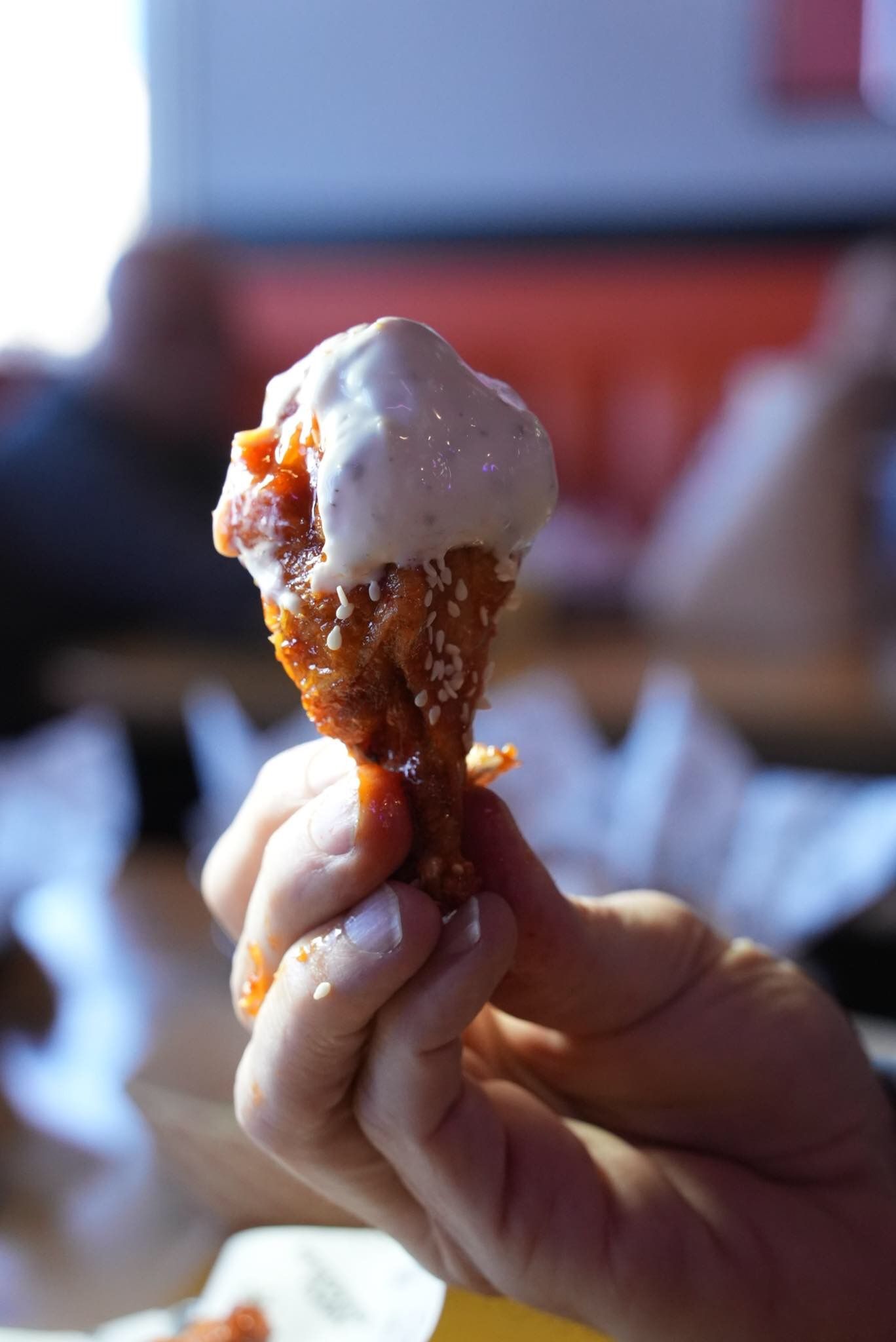 A hand holds a crispy fried chicken drumstick topped with a generous dollop of creamy white dipping sauce.