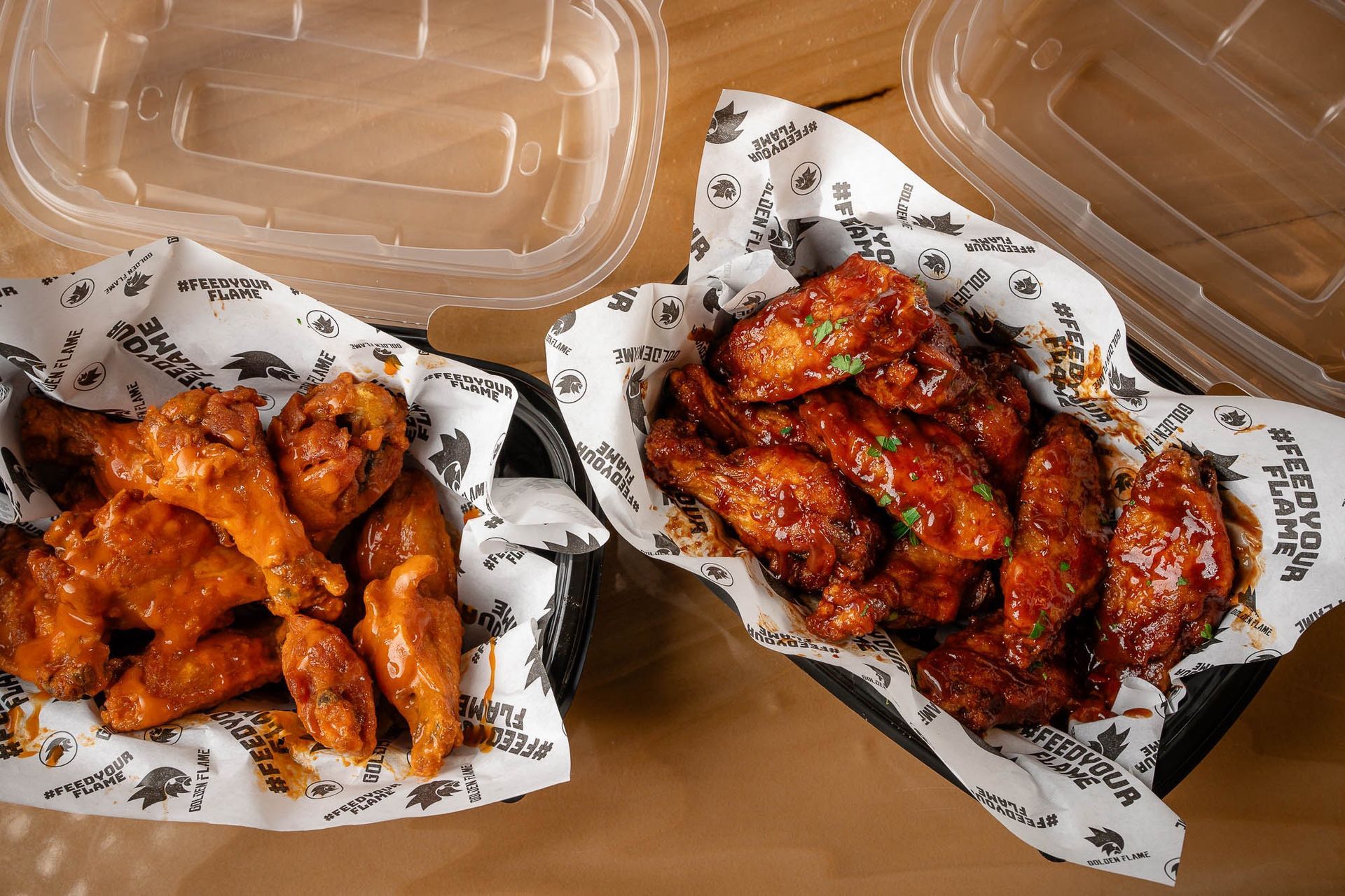 Two containers of buffalo chicken wings on white paper liners, one with a lighter sauce and one with a darker red sauce.