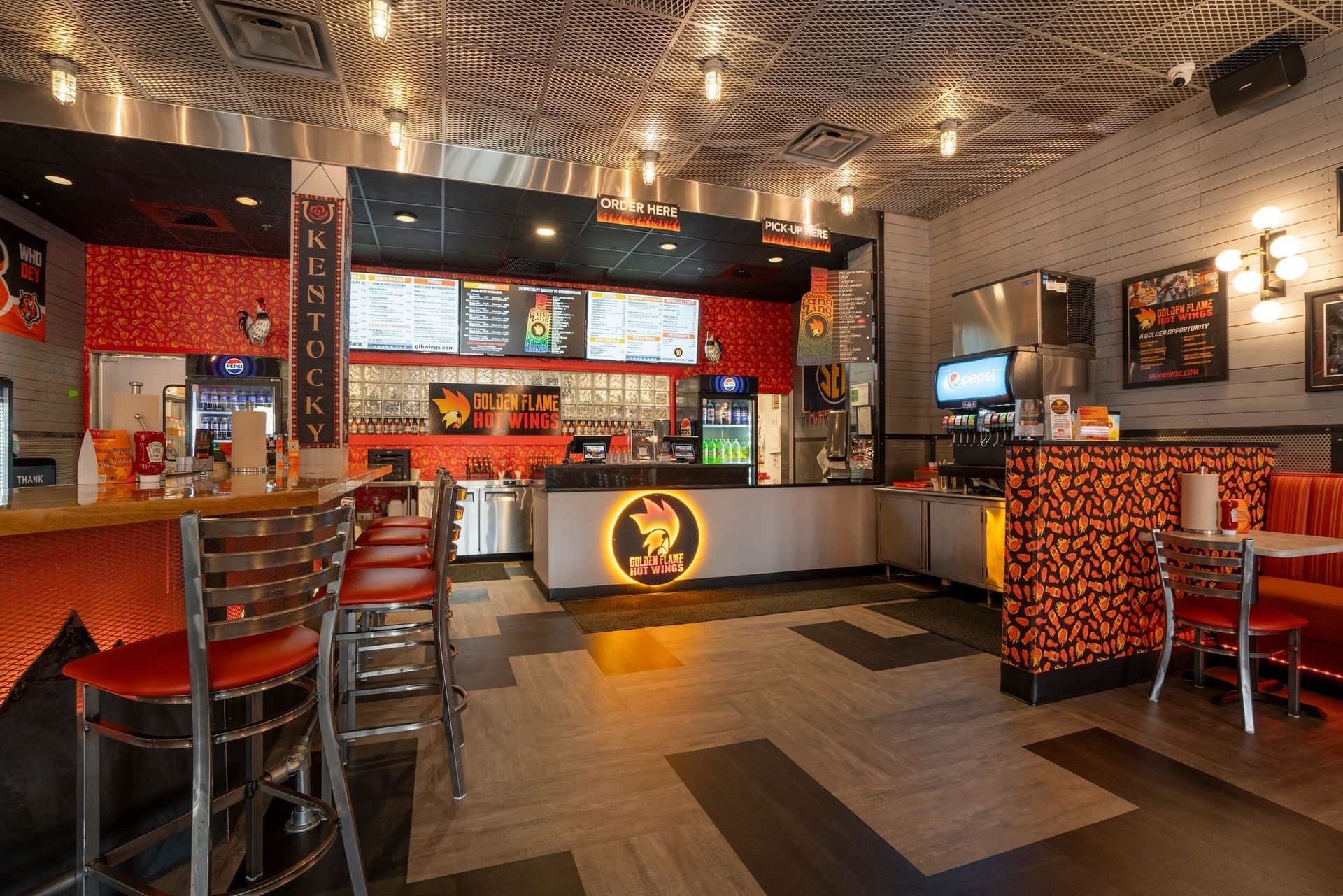 The interior of a restaurant featuring a bar, seating area, patterned ceiling, and a food service counter with a logo.