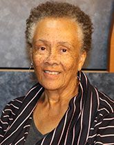 Smiling person wearing a black and white striped scarf over a dark shirt against a blue, textured background.