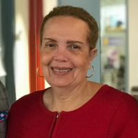 A smiling woman with short, brown hair and silver hoop earrings, wearing a red top against an indoor background.