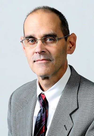 Headshot of a person wearing glasses, a patterned gray suit, a white collared shirt, and a dark red patterned tie.