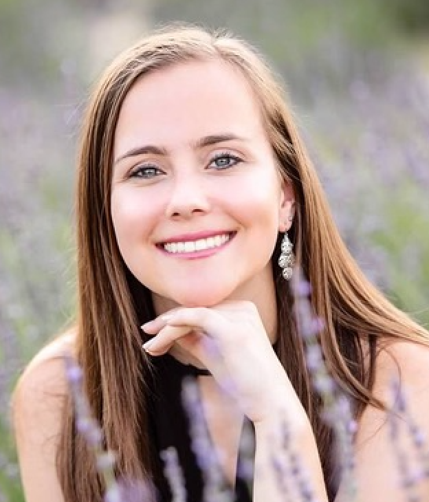 Portrait of a smiling person with long brown hair, resting their chin on their hands in a lavender field.