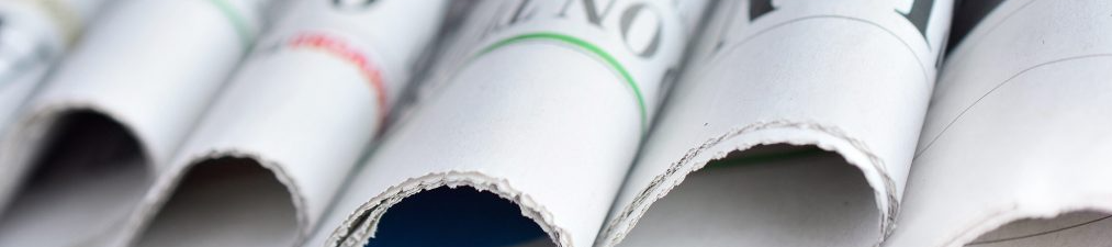 Close-up of stacked newspapers with white pages and blurred text, showing their curved edges and distinct folds.