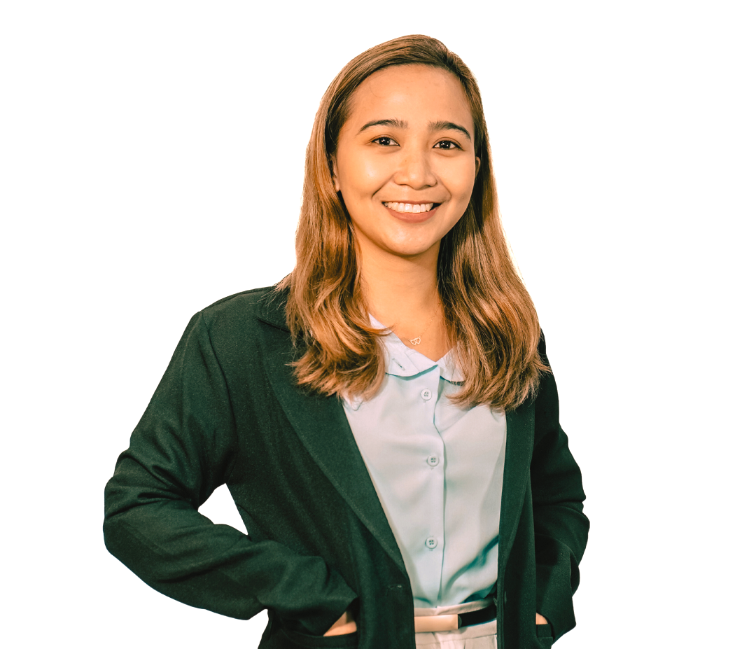 A person with long hair smiles, wearing a green blazer over a light blue collared shirt, hands resting on their hips.