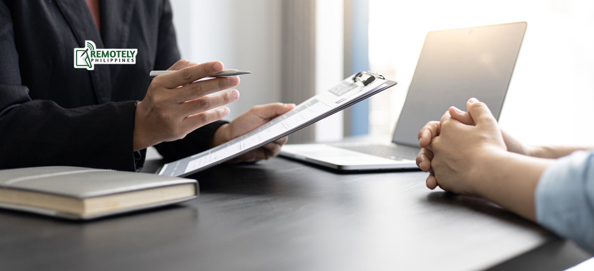 A person in a suit points to a document while interviewing another person in an office.