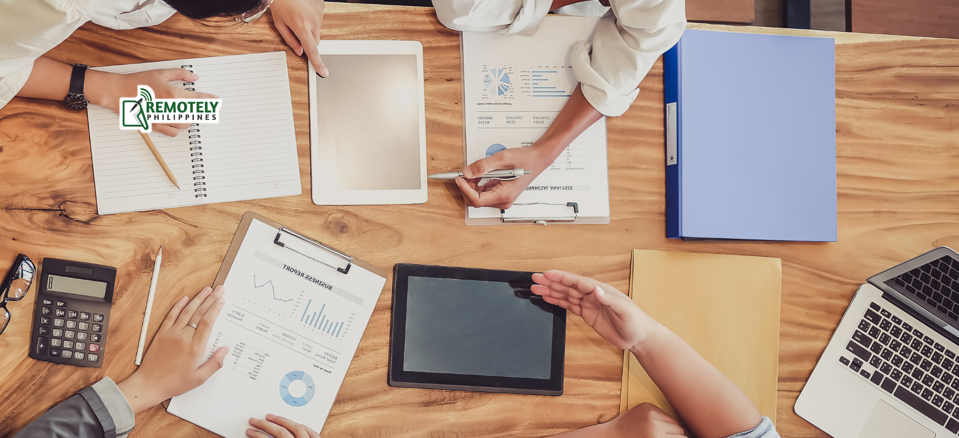 People collaborating around a table with papers, a tablet, and a laptop.