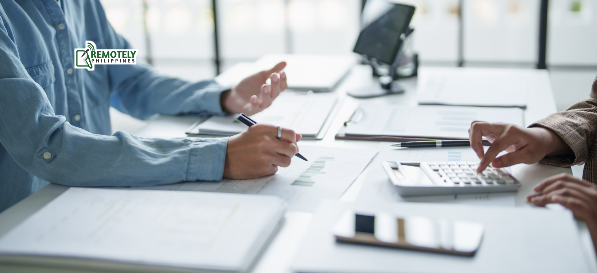 Two people reviewing financial documents and using a calculator at an office desk.
