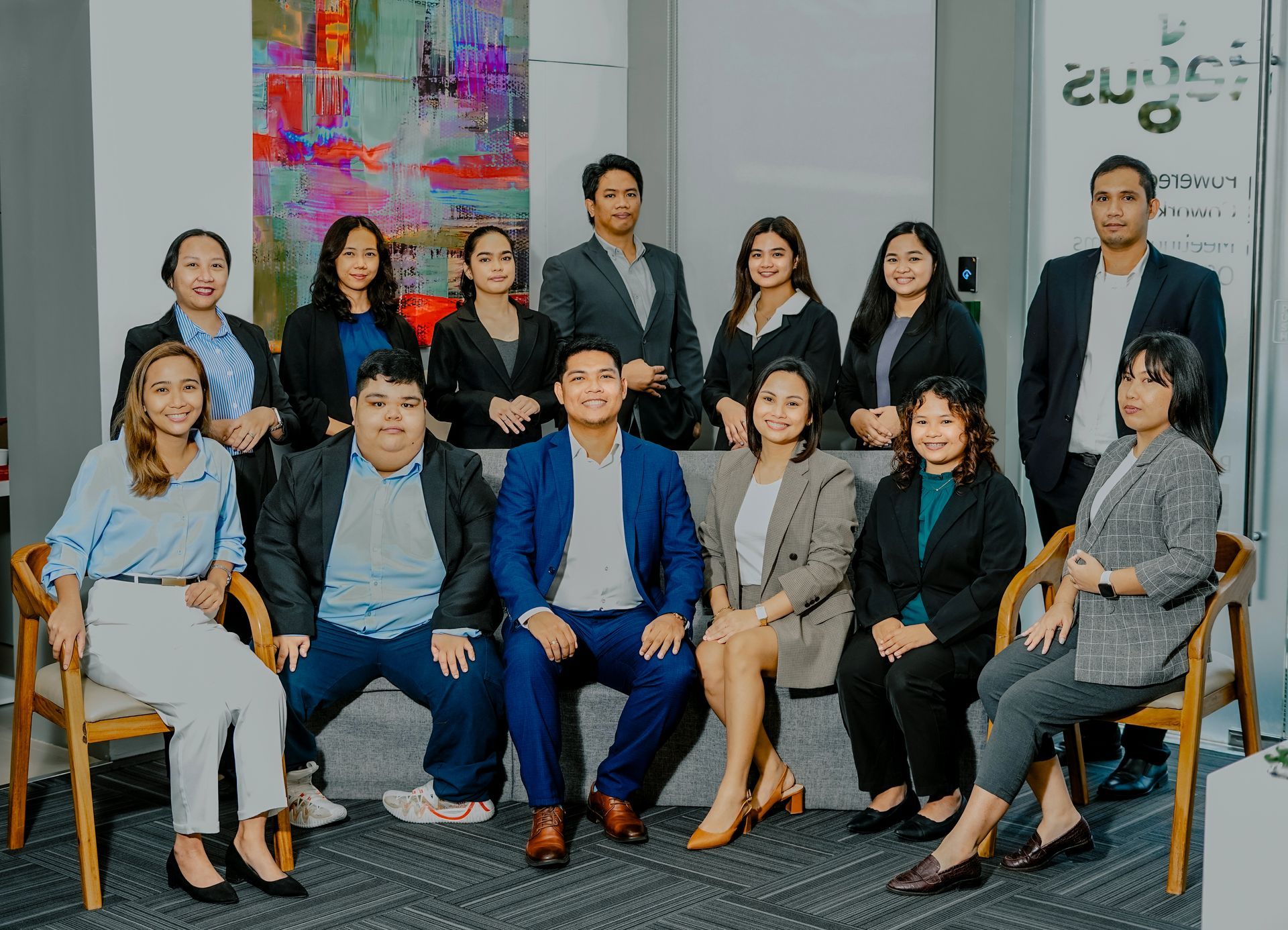 Group of people in business attire posing in an office setting with art on the wall.