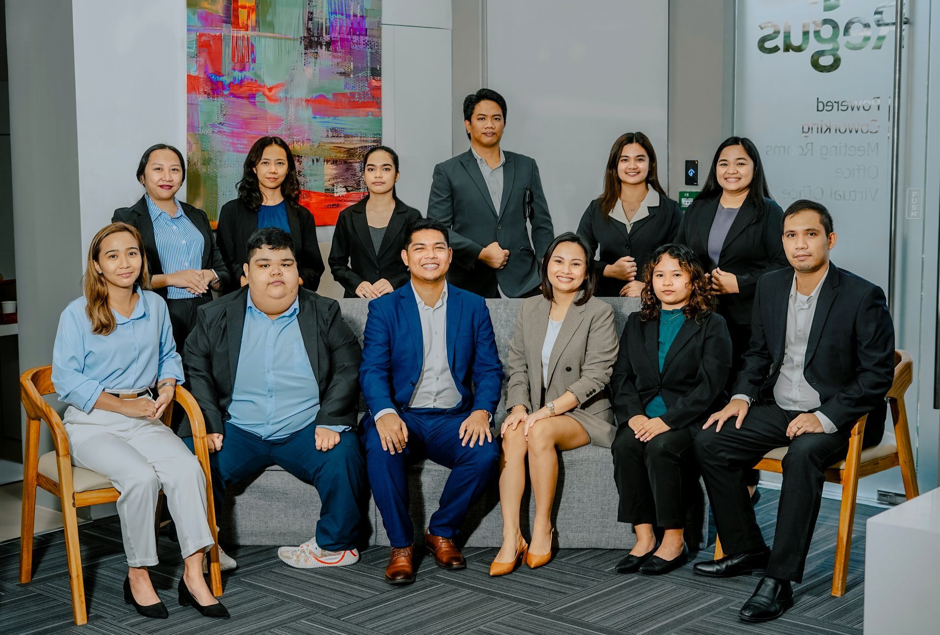 Group photo of a business team, smiling, in an office setting. They are wearing business attire in front of colorful artwork.