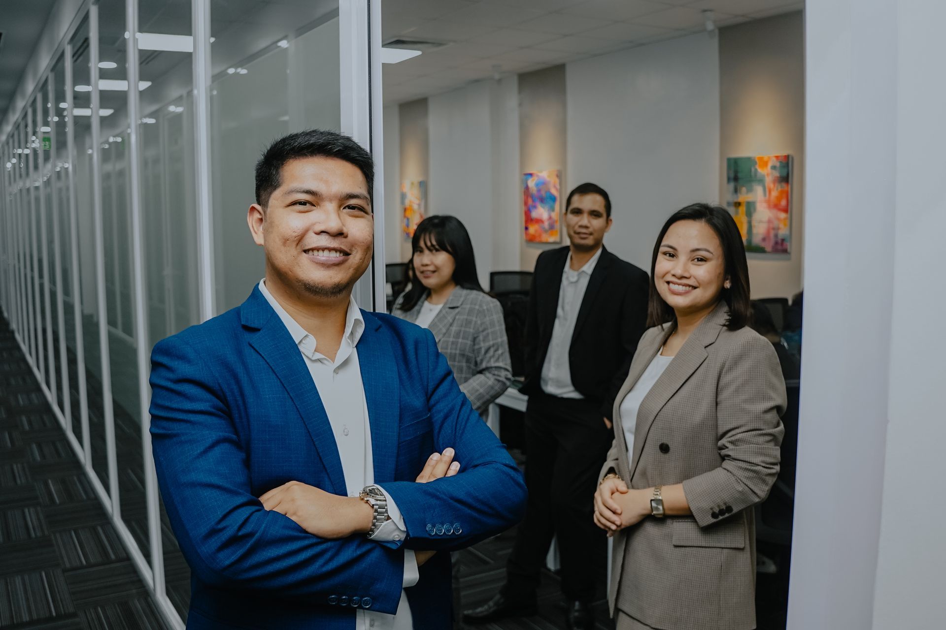 Business team, man in blue jacket in the foreground, office setting, colleagues in the background.