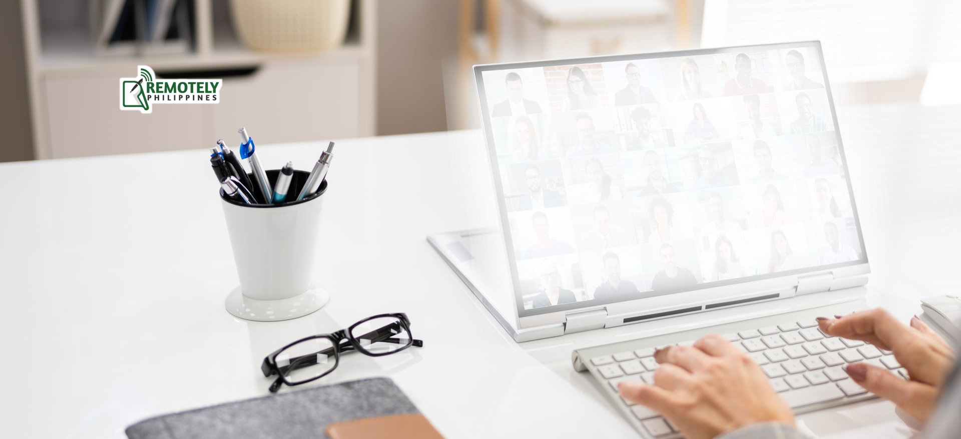 Person typing on a laptop at a white desk with pens, glasses, and a notepad.