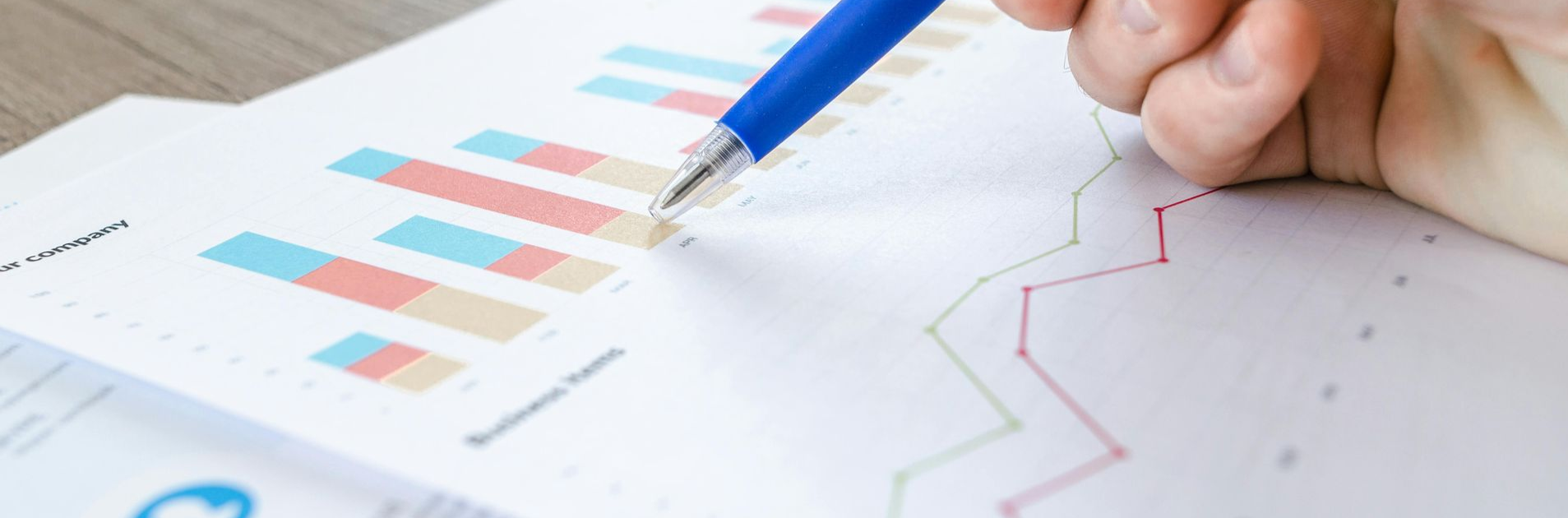 Person's hand with blue pen points to a bar graph and line graph on white paper.