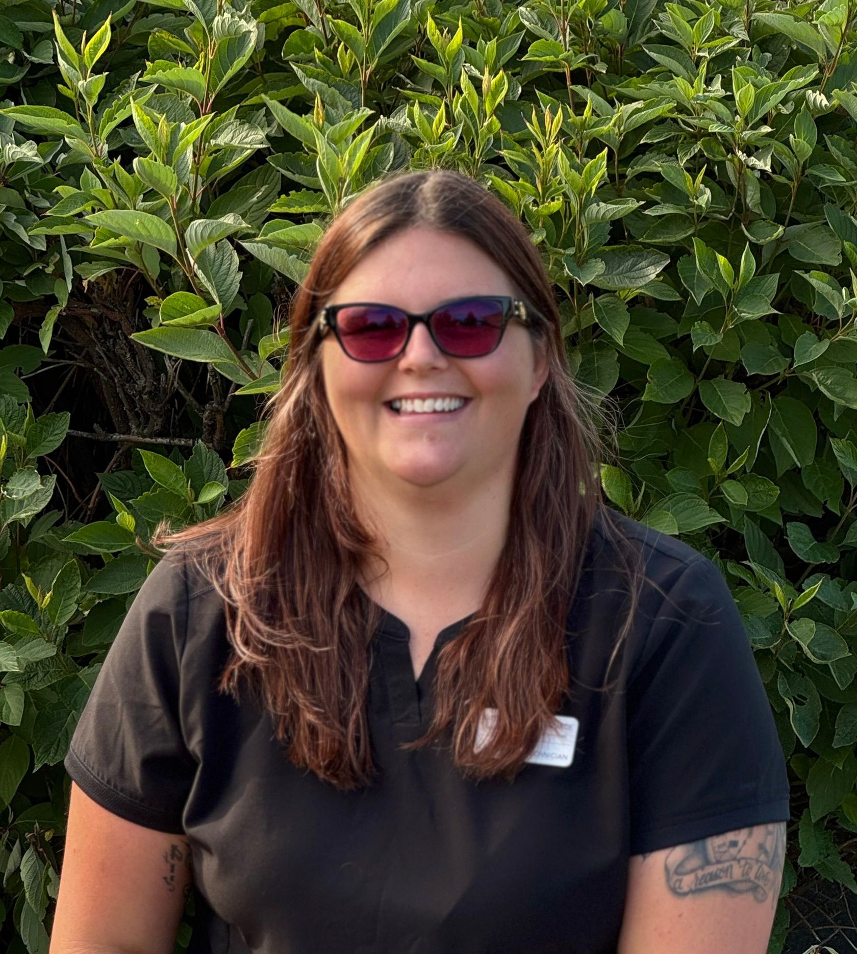 A woman is leaning against a wall with her arms crossed and smiling.