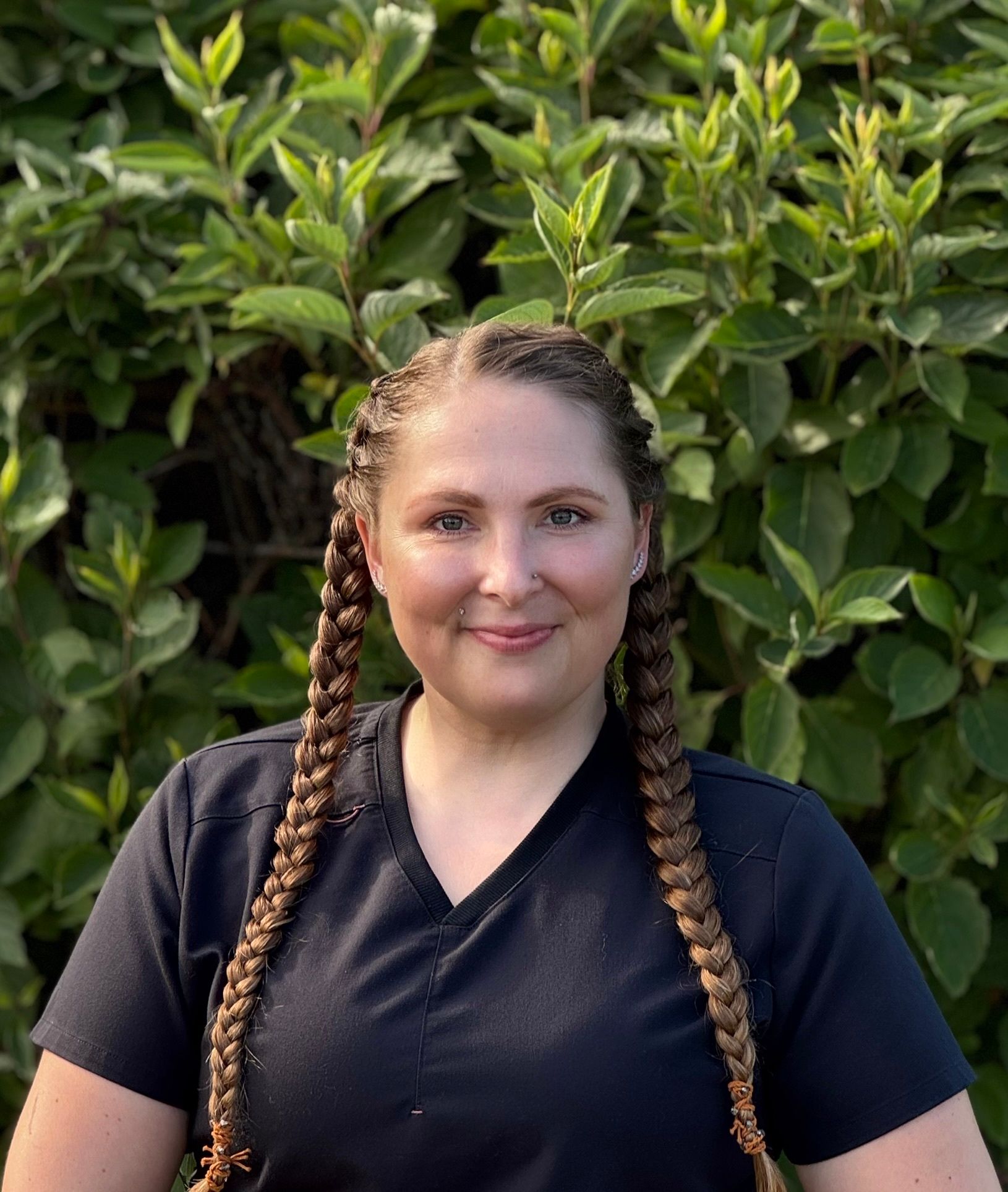 A woman is leaning against a wall with her arms crossed and smiling.