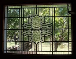 Decorative black metal window grille framing a view of trees and a sunlit yard outside
