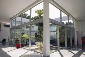 Modern glass-walled courtyard with a white overhang and potted plants in bright sunlight