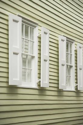 White shutters on two windows against pale green horizontal siding.