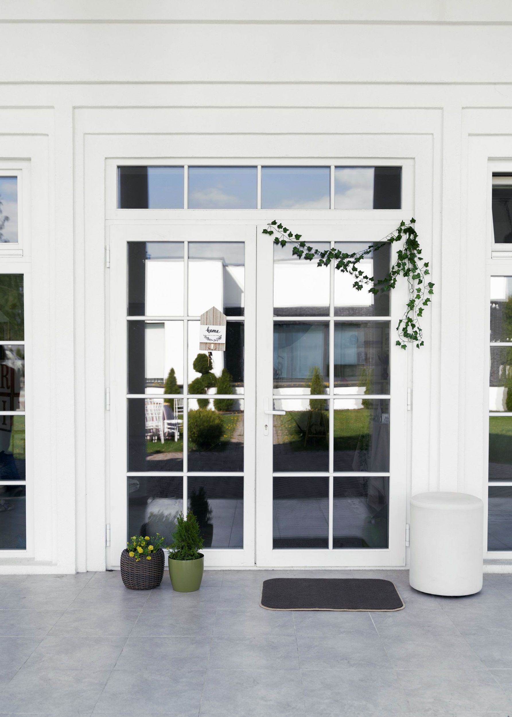 White French doors with glass panes, potted plants, and a doormat on a porch.
