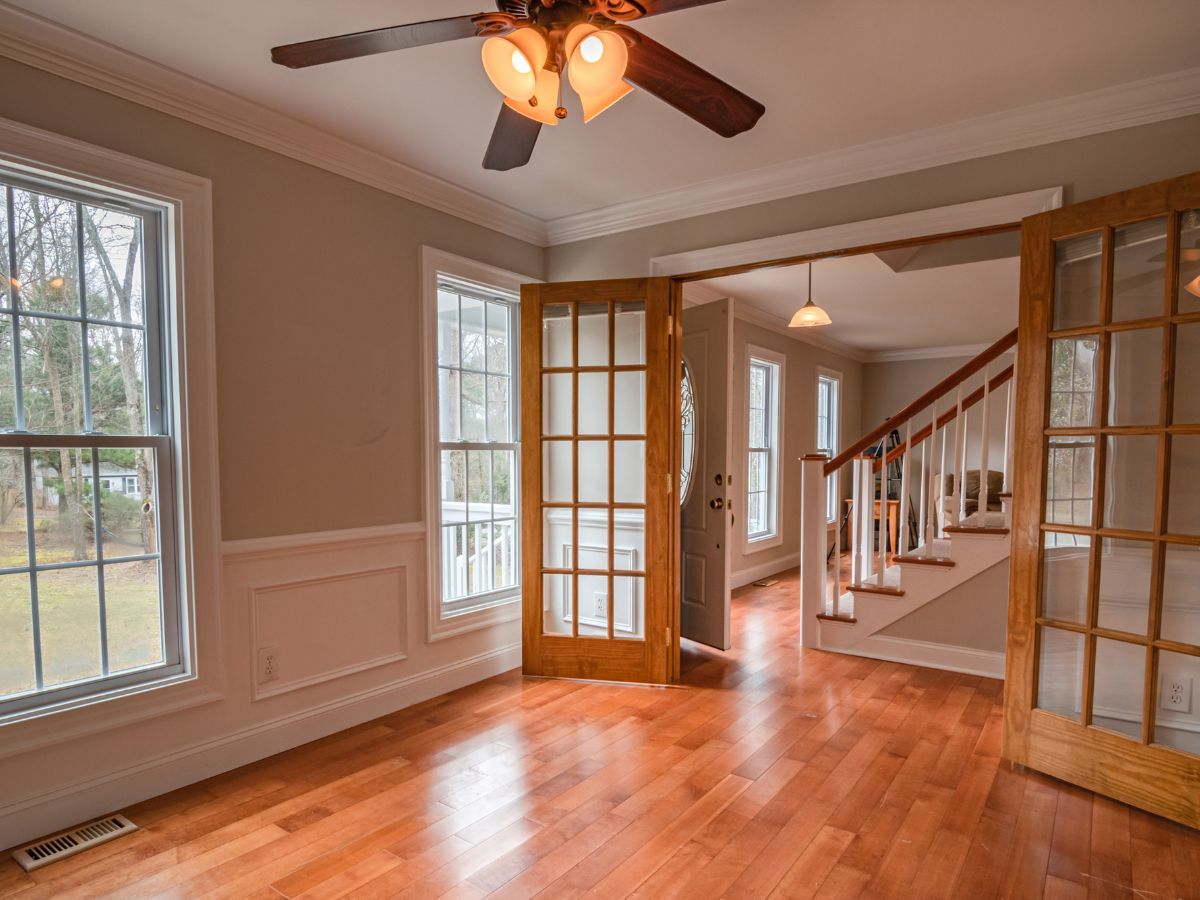 Empty room with hardwood floors, French doors, and windows, lit by a ceiling fan and warm natural light