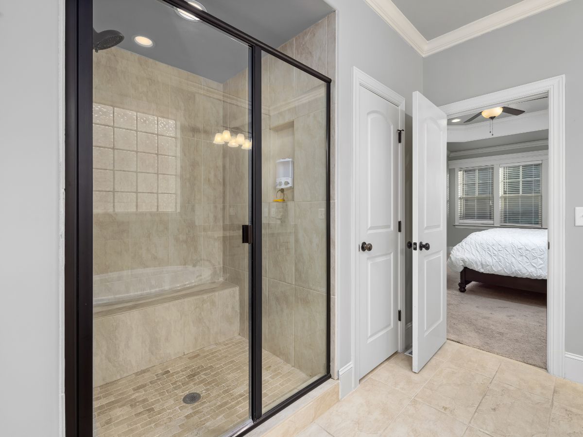Modern bathroom with glass-enclosed shower and a doorway to a bedroom beyond.
