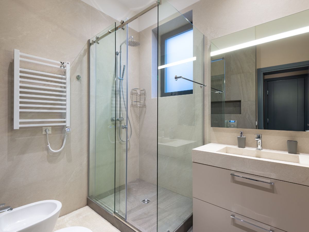Modern bathroom with glass shower, white towel rack, sink, and large mirror in neutral tones