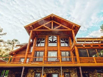 Wooden lodge with large windows and a peaked roof against a bright sky