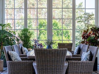Sunlit garden room with wicker chairs, cushioned seating, and lush indoor plants by tall windows