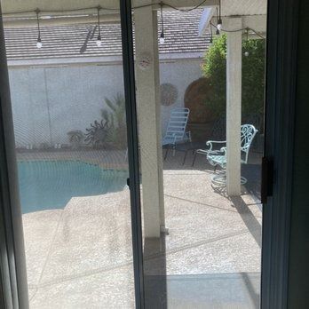 Patio view through sliding doors of a backyard pool, white chairs, and a covered patio area