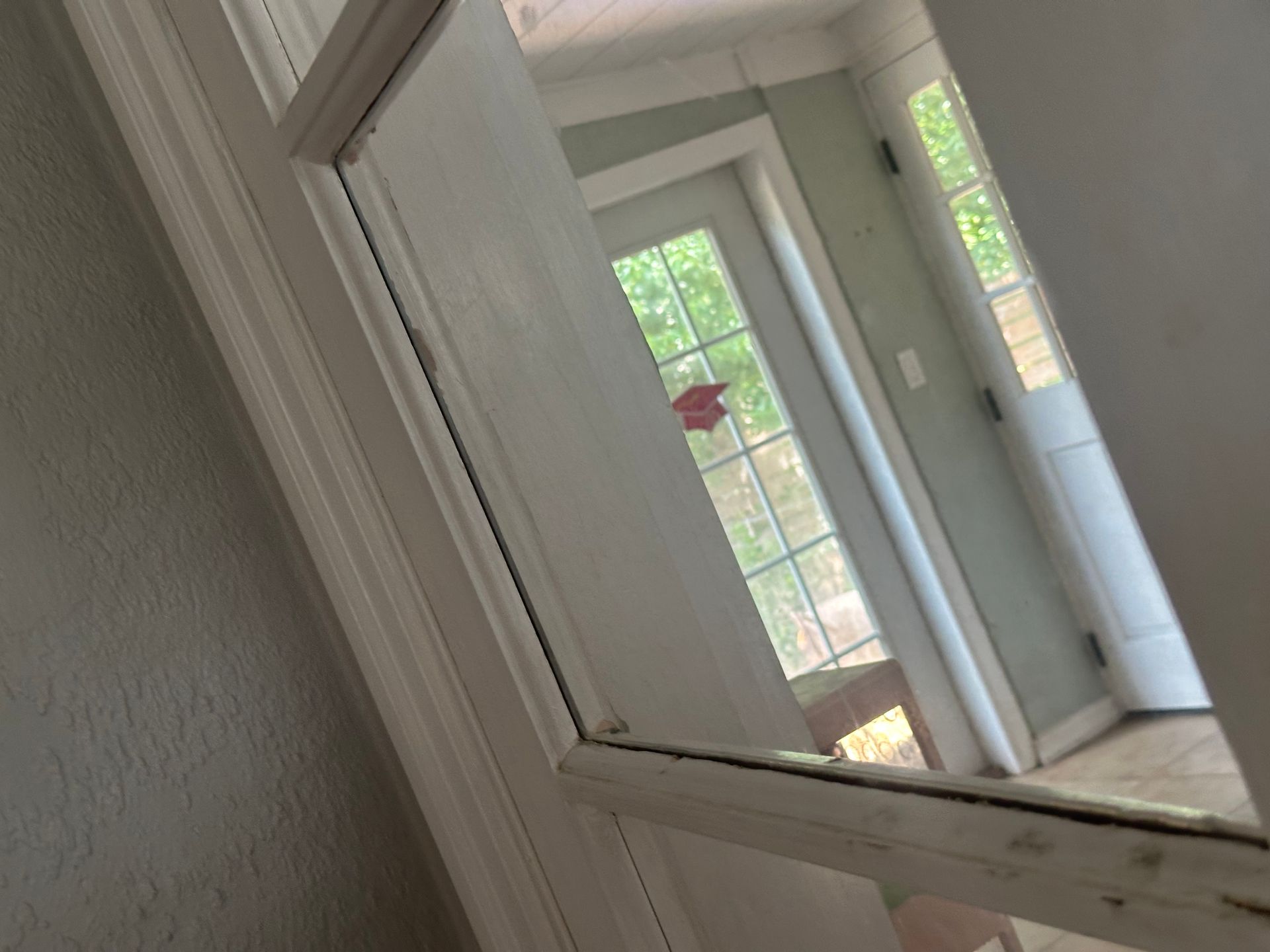 White hallway with a tilted mirror reflecting a bright doorway and window.