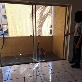 Man standing by a sliding glass door, looking out at a sunlit patio with a bag on the floor.