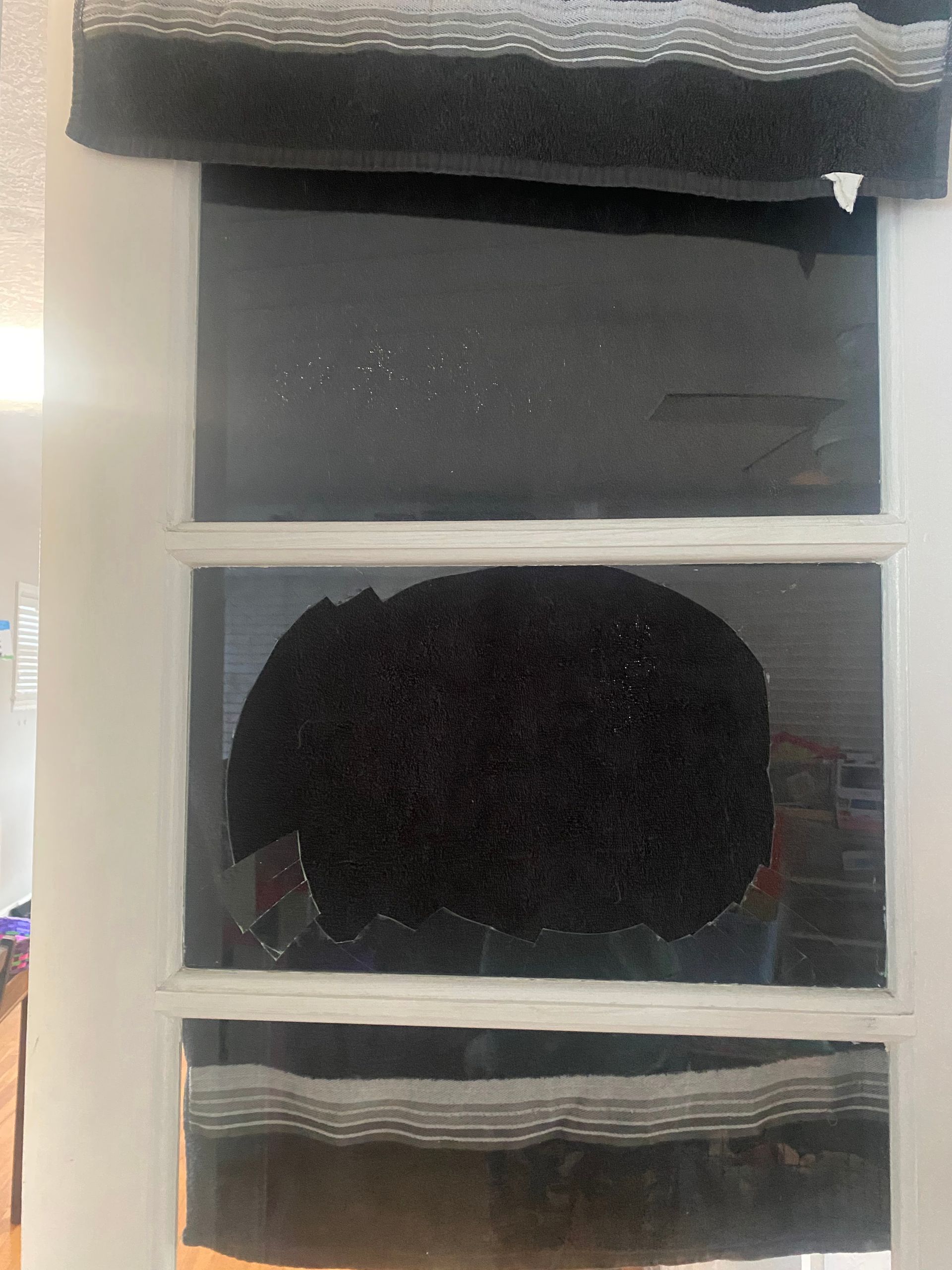 Dark window with white frame and partially closed blinds, showing a dark rounded object behind the glass