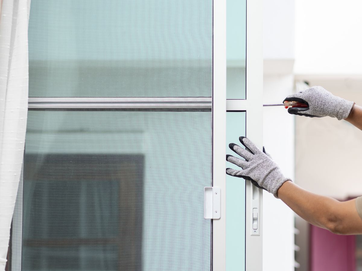 Gloved hands using tools to install a white door frame beside a glass sliding door