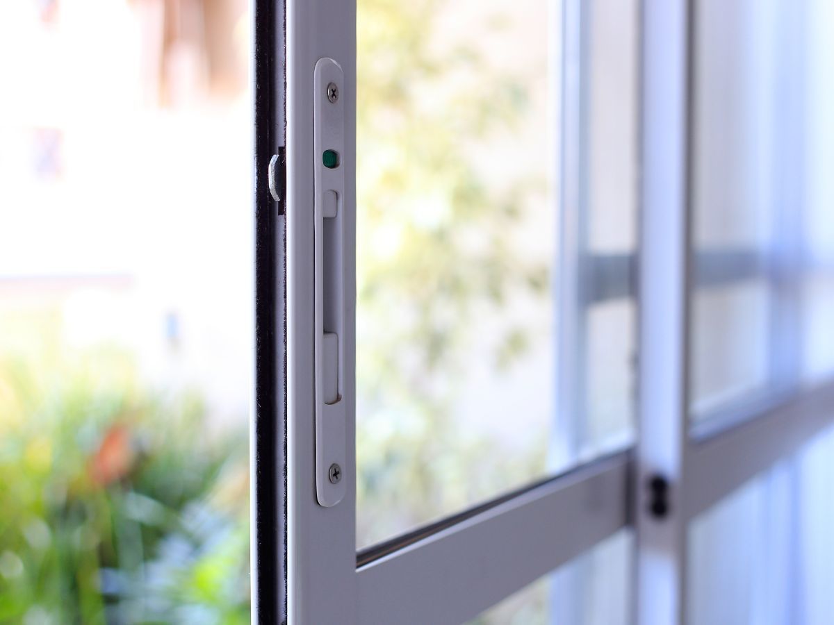 Close-up of a glass door edge with metal latch and handle against a bright blurred background
