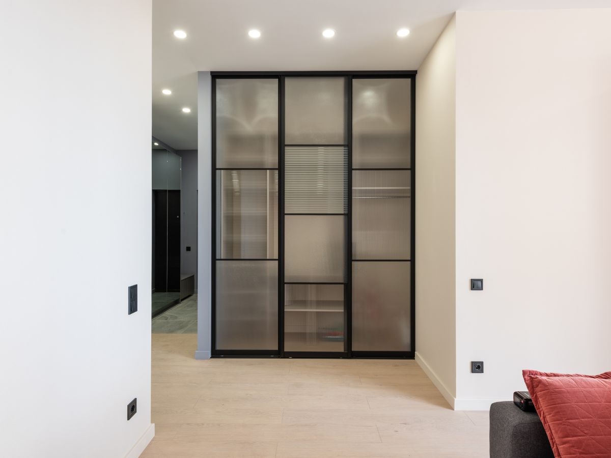 Modern room with black-framed glass wardrobe doors, recessed ceiling lights, and light wood flooring
