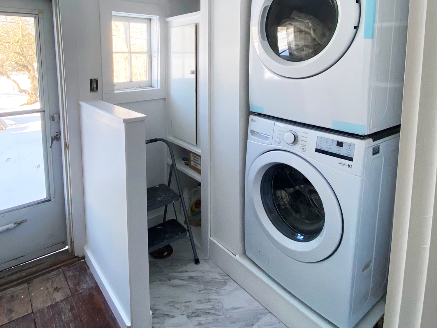 A new washer and dryer are stacked on top of each other in a laundry room with custom cabinetry by JG Services.