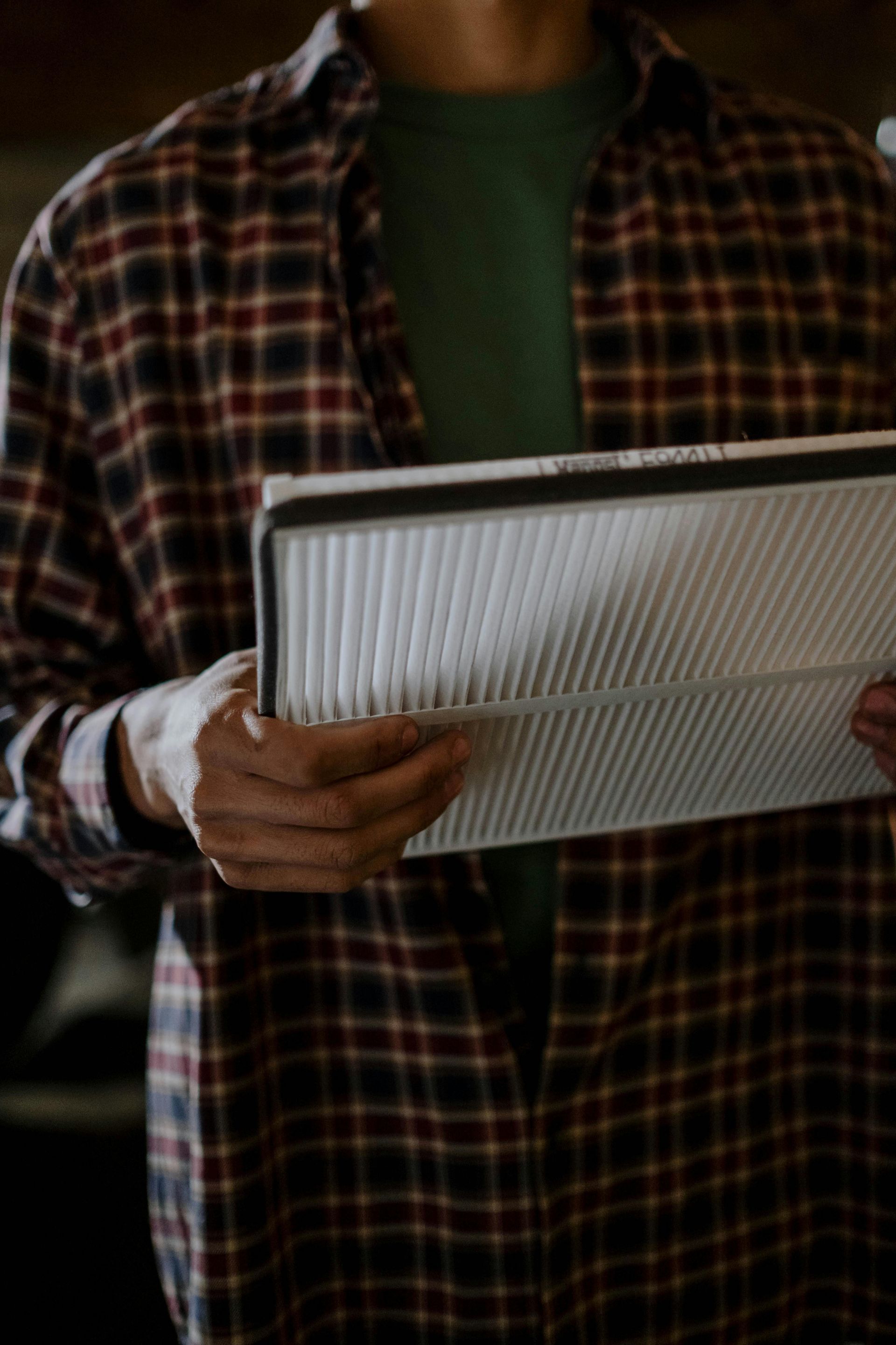 Person in plaid shirt holding a white air filter, likely inspecting it.