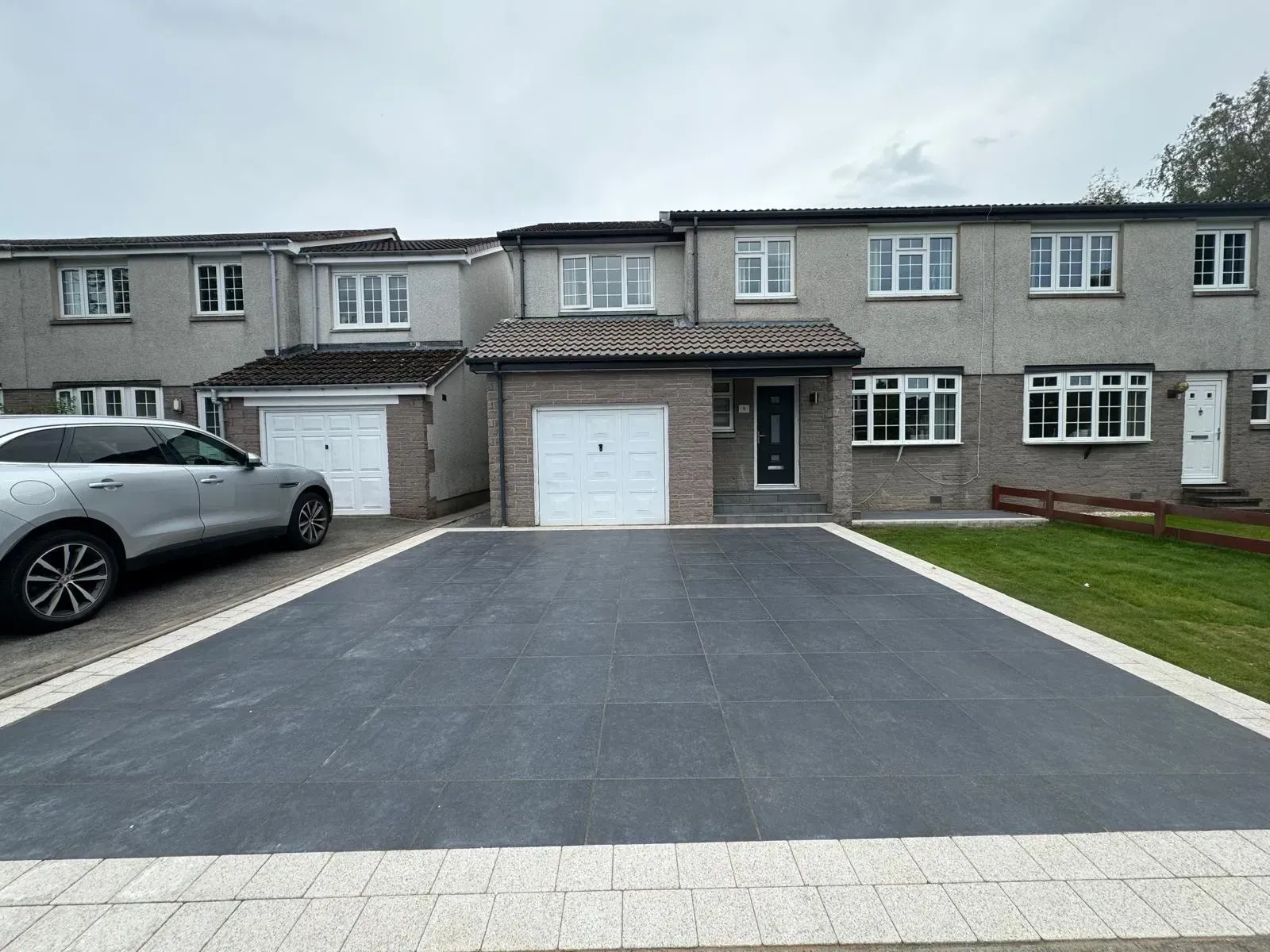 Row of townhouses with gray facades, driveways, and manicured lawn.