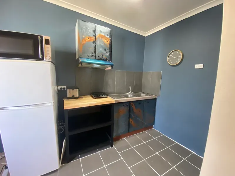 A kitchen with a refrigerator , sink , microwave and clock on the wall.