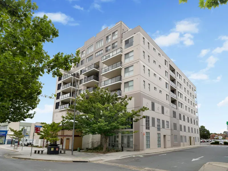 A large apartment building is sitting on the corner of a city street.
