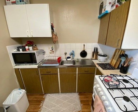 A kitchen with a sink , stove , microwave , and trash can.