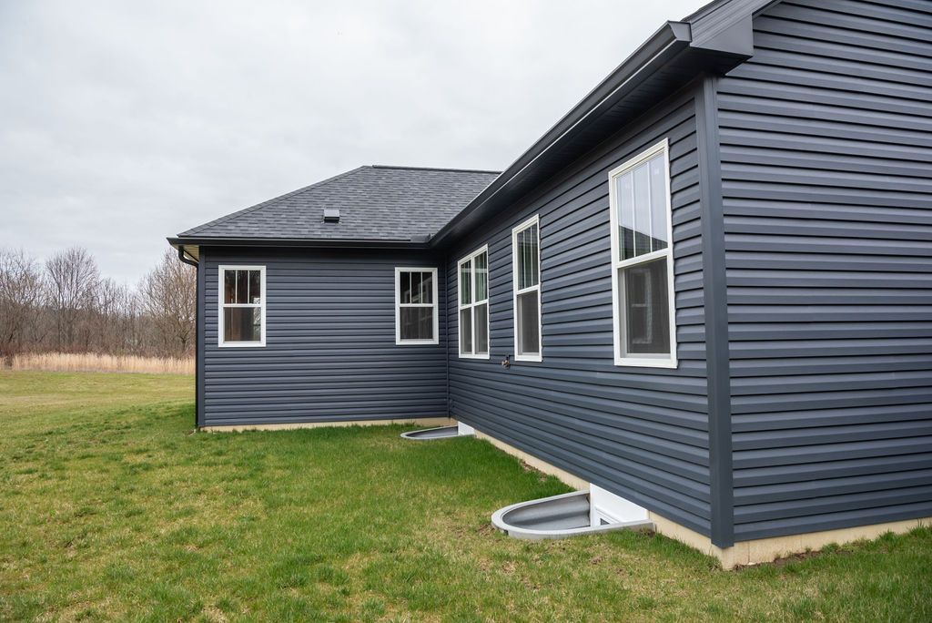 A black house with a lot of windows is sitting in the middle of a grassy field.