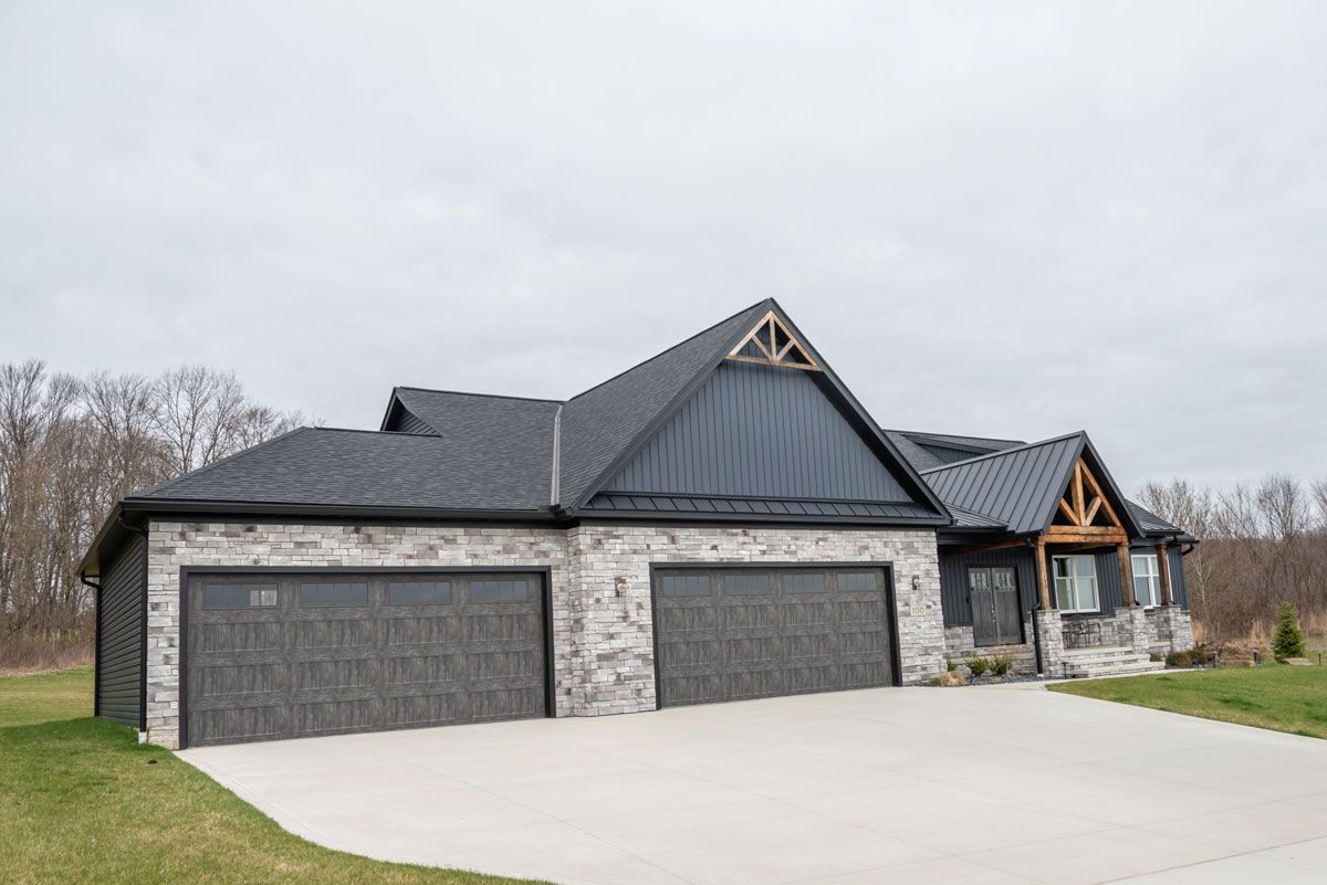 A large house with three garage doors and a black roof.