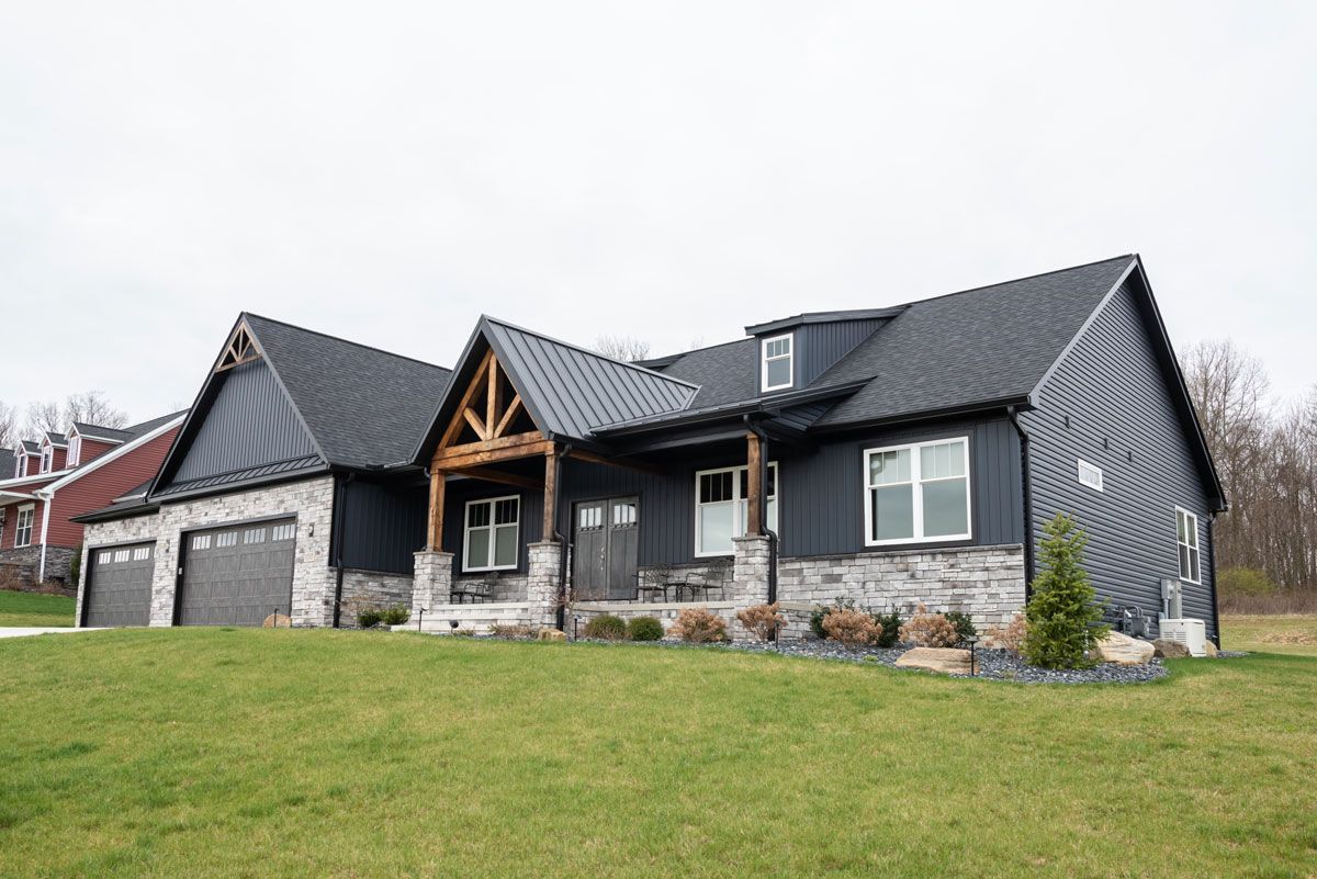 A large house with a black roof is sitting on top of a lush green field.