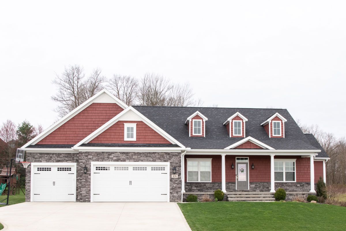 A red house with a black roof and white garage doors