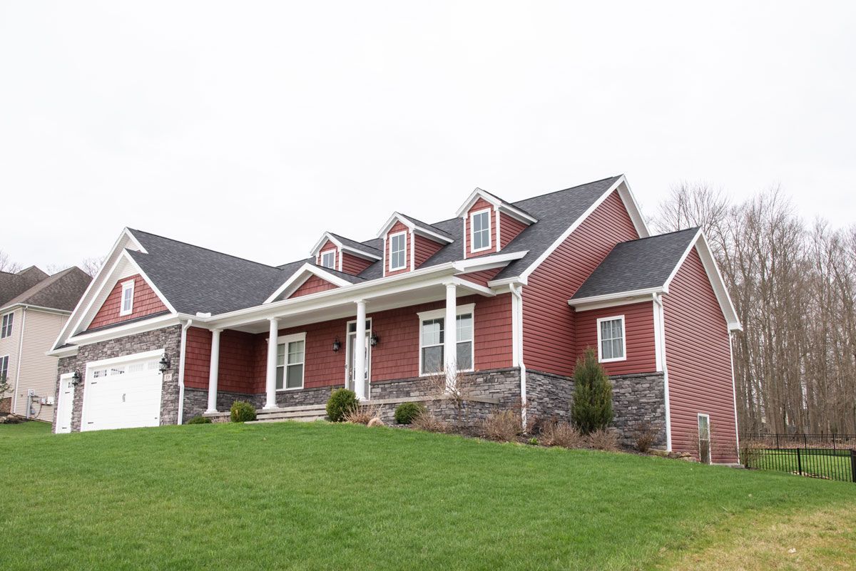 A large red house with a black roof is sitting on top of a lush green hillside.