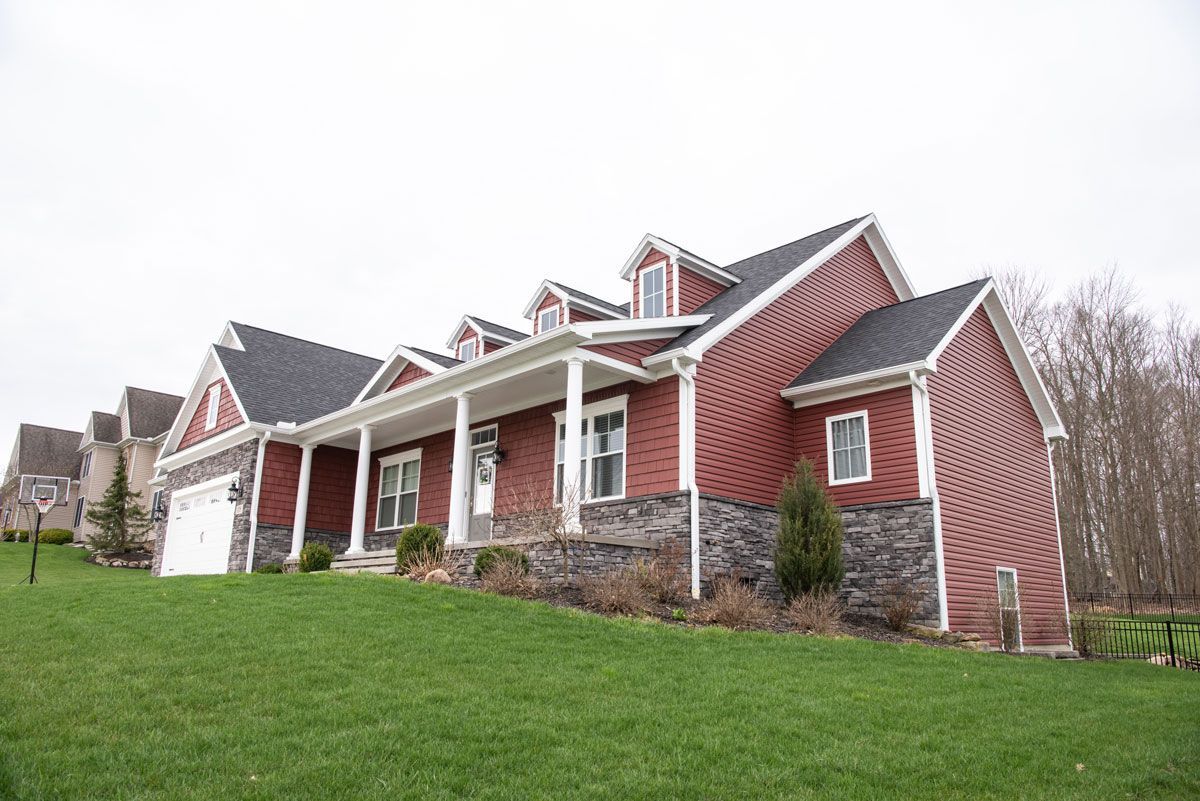 A large red brick house with a large porch is sitting on top of a lush green hillside.